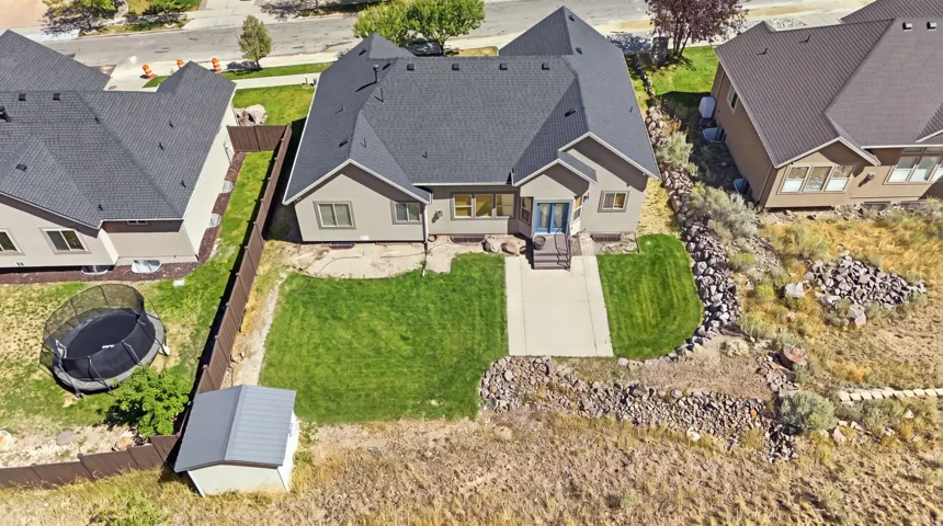 Rear exterior featuring a concrete patio, landscaped lawn, wood fence, and storage shed