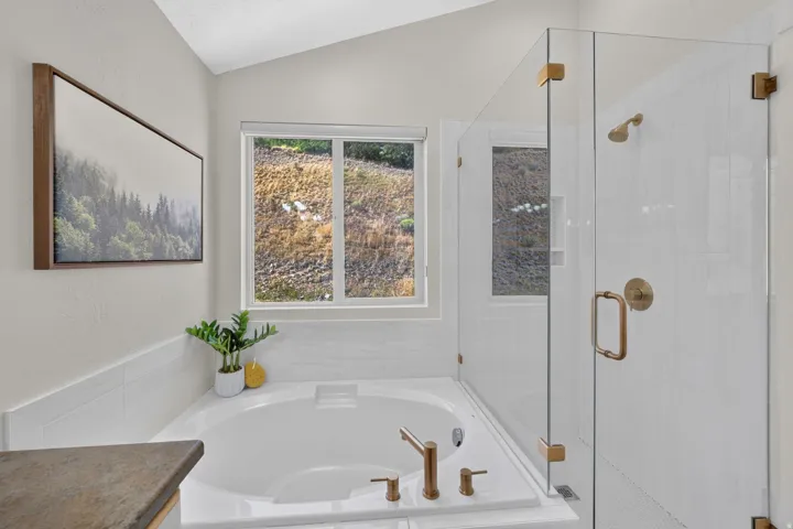 Soaking tub with bronze-finish fixtures, white tile surround, and a clear glass walk-in shower