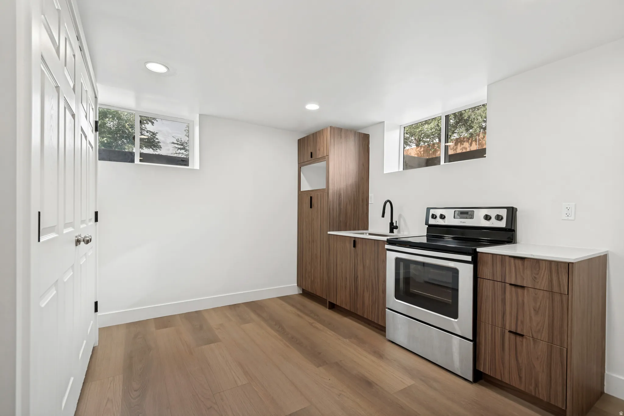 Wood-finish flooring, white walls, recessed lighting, wood cabinetry, and stainless steel appliances