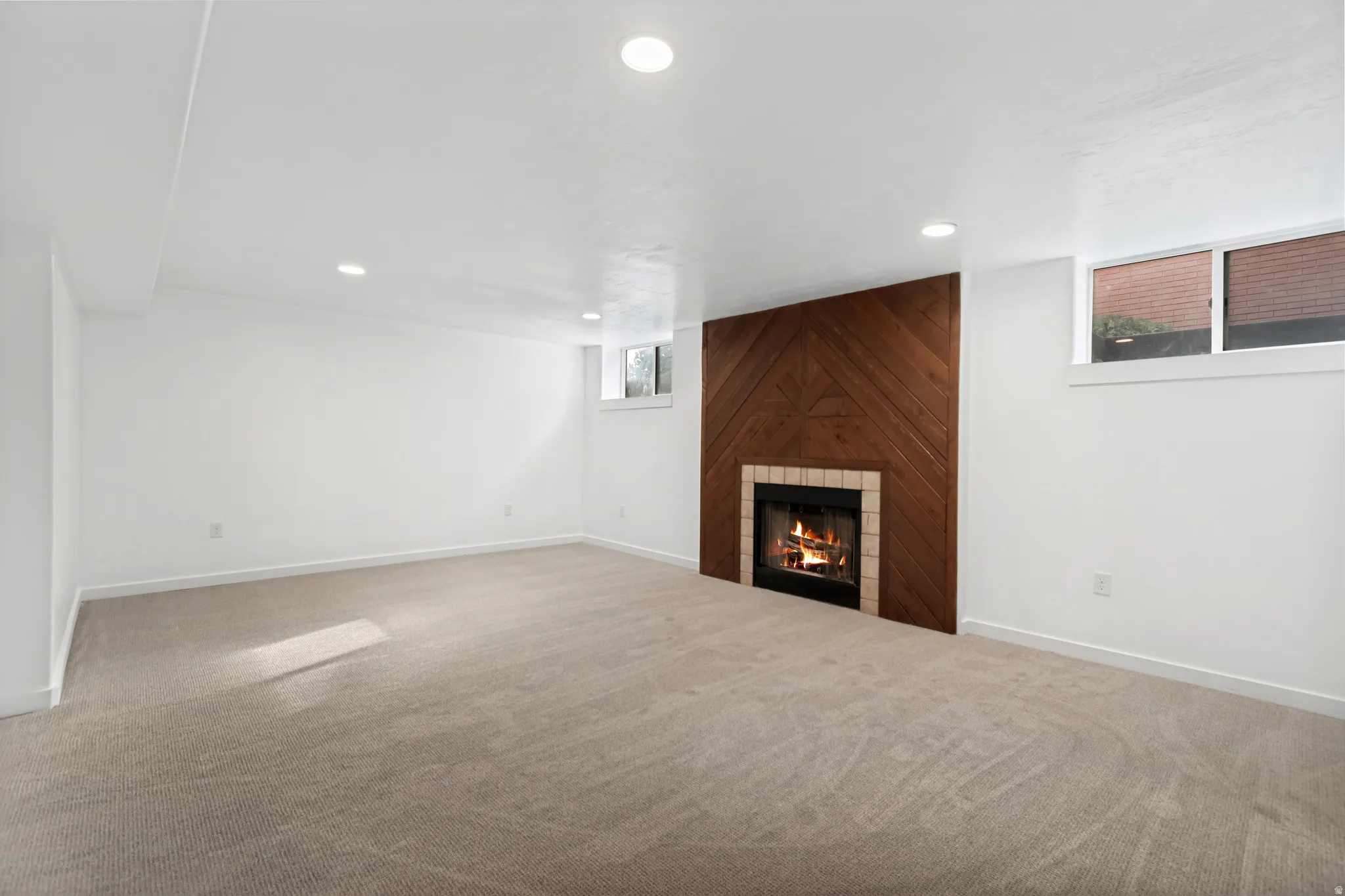 Recessed lighting illuminates a spacious room featuring a fireplace with a wood-paneled accent wall, a tiled hearth, and carpet flooring