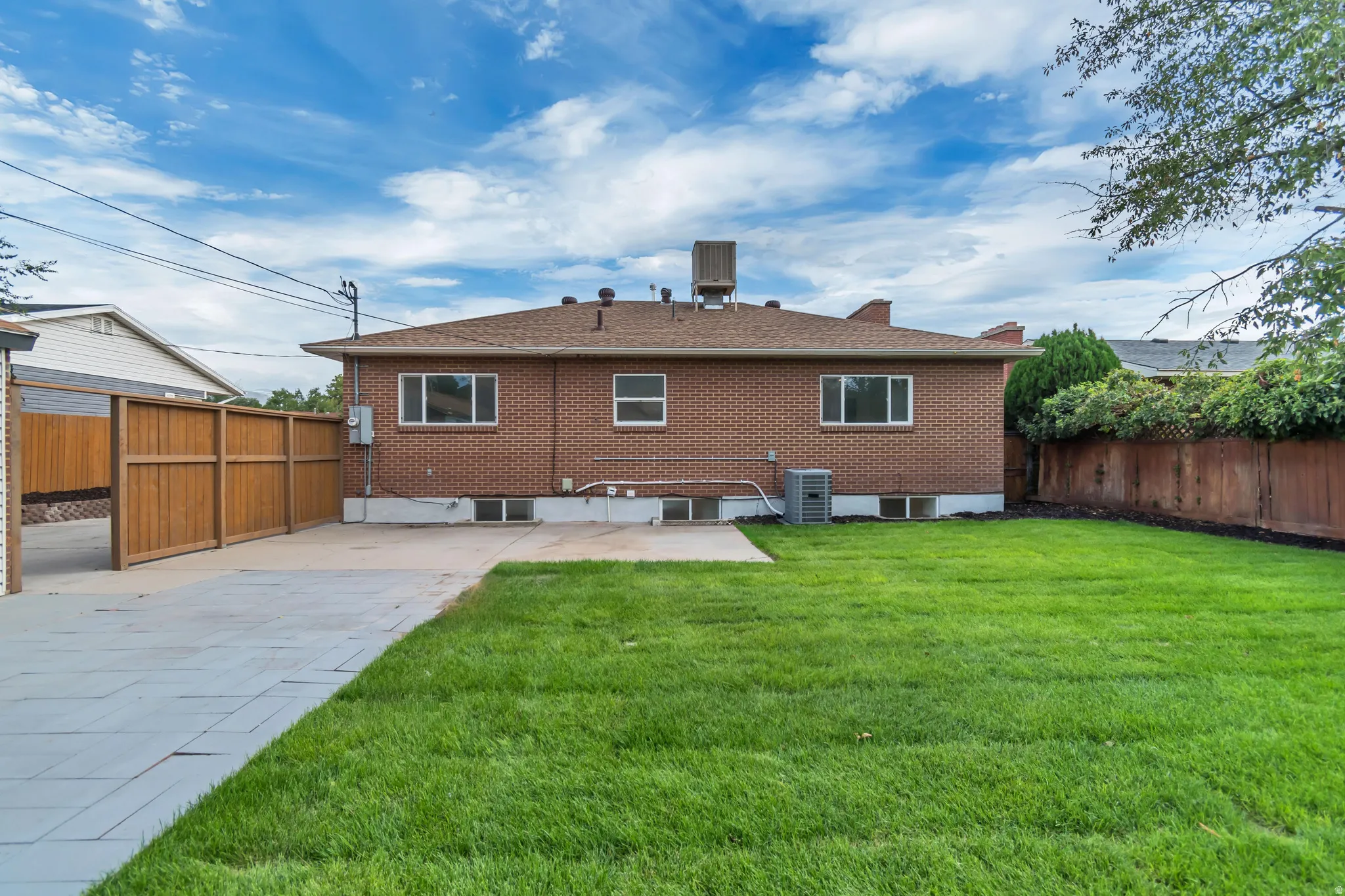 Expansive green lawn, brick exterior, paved patio area, and wood fencing