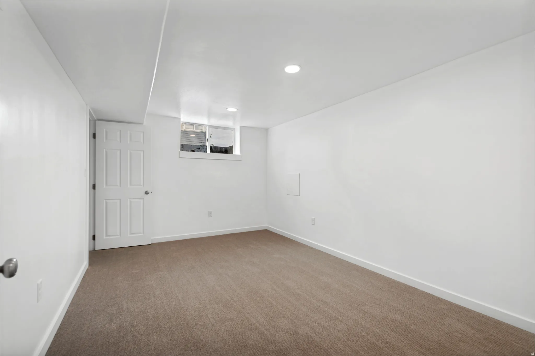 Recessed lighting, white walls, light brown carpet flooring, and a white six-panel door