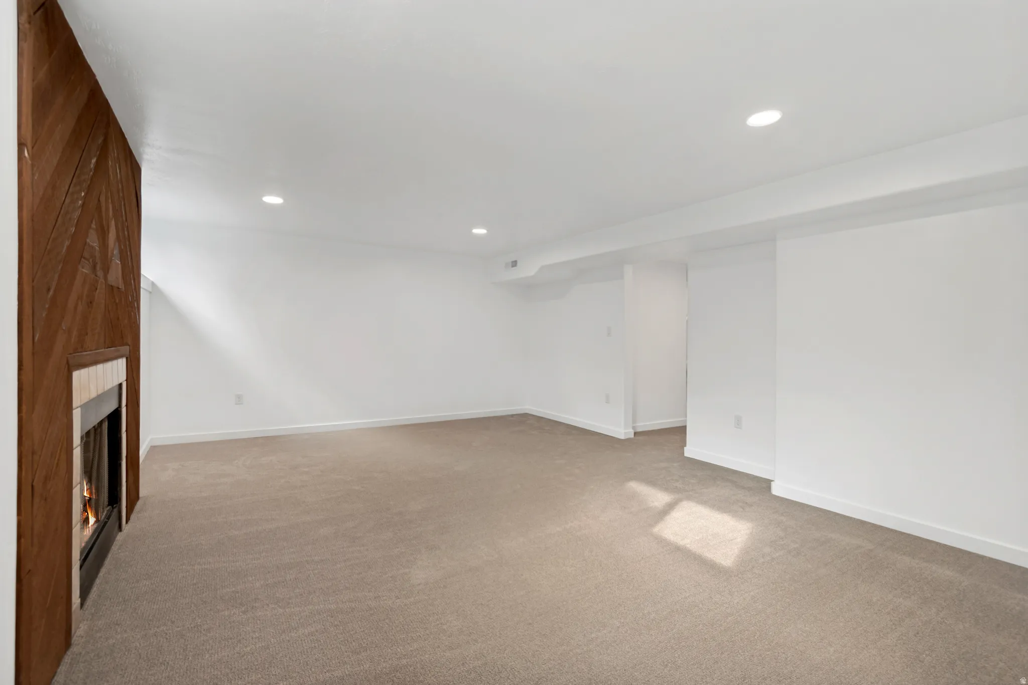 Recessed lighting, wood-paneled accent wall, built-in fireplace with hearth, plush carpeting, and crisp white wall finishes