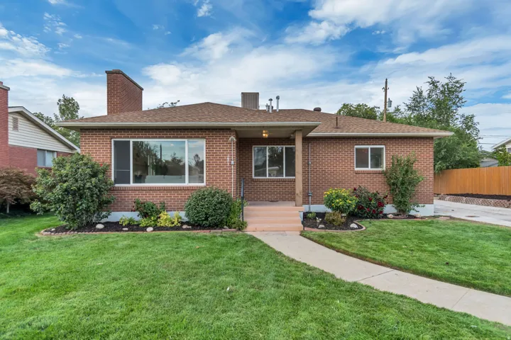 Brick exterior with a brown shingle roof, concrete pathway, and landscaped garden beds