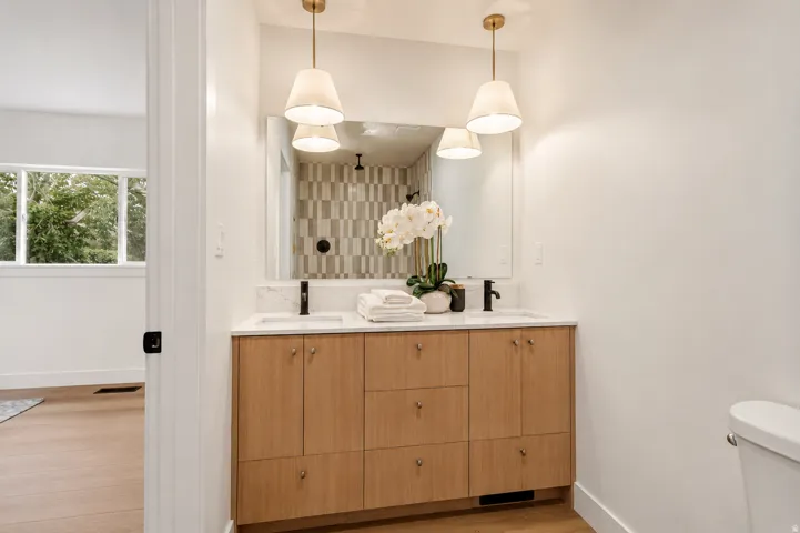Double vanity with light wood-finish cabinetry, white stone-finish countertop, dual under-mount sinks, and matte black fixtures