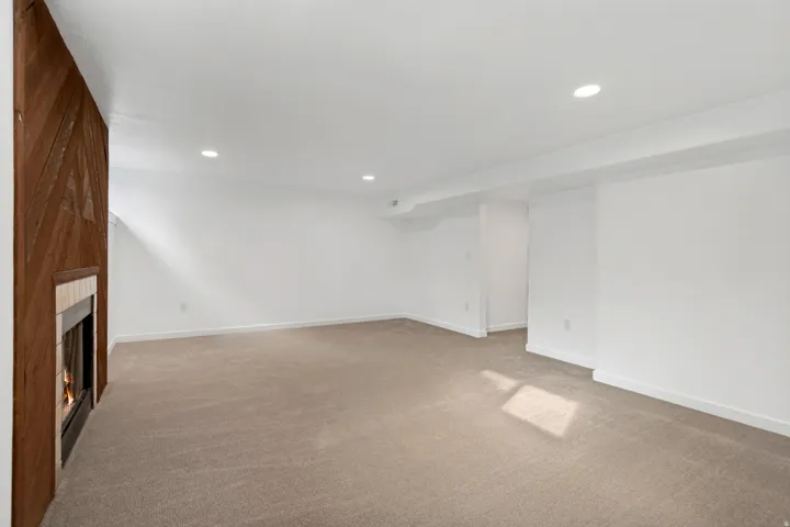 Recessed lighting, wood-paneled accent wall, built-in fireplace with hearth, plush carpeting, and crisp white wall finishes