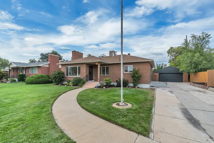 Brick exterior with a detached garage, concrete driveway, front yard with mature landscaping, and a flag pole