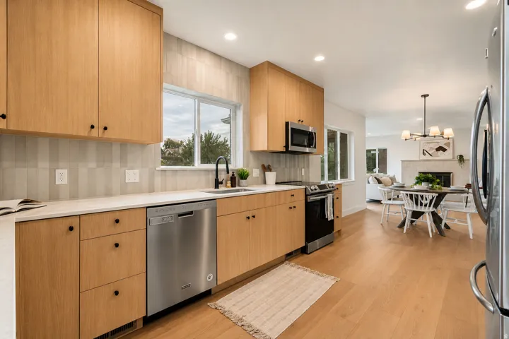 Light wood-finish cabinetry, stainless steel appliances, a white countertop, and a tile backsplash