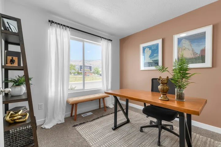 Carpeted flooring, window with natural light, built-in shelving, wood-finish desk with metal base, and a statement accent wall