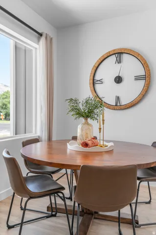 Wood-finish flooring with a round wooden dining table, set against light-colored walls and a window with sheer curtains