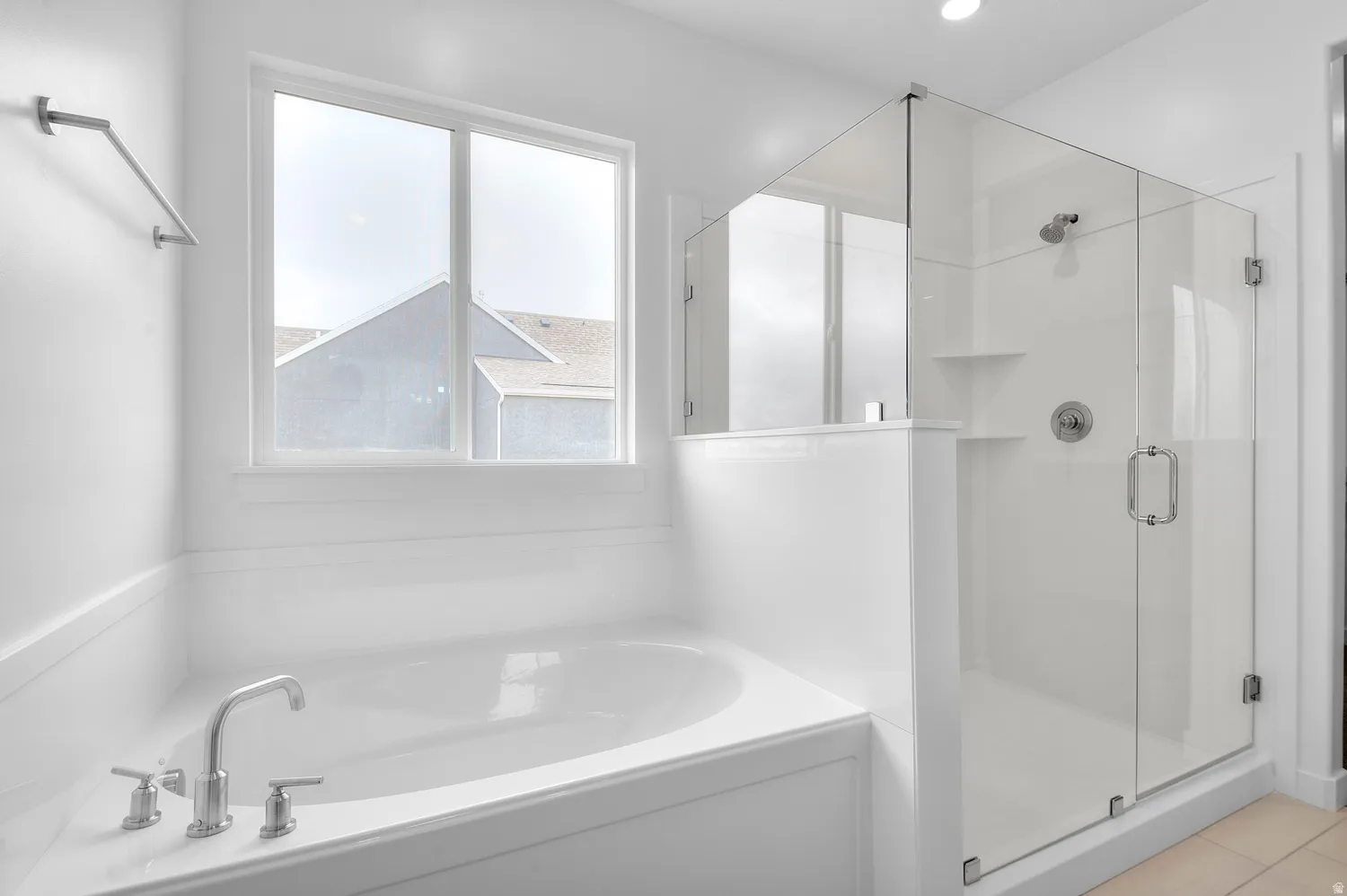 Deep soaking tub with polished chrome fixtures, glass-enclosed shower with built-in shelving, white tiled walls, and recessed lighting
