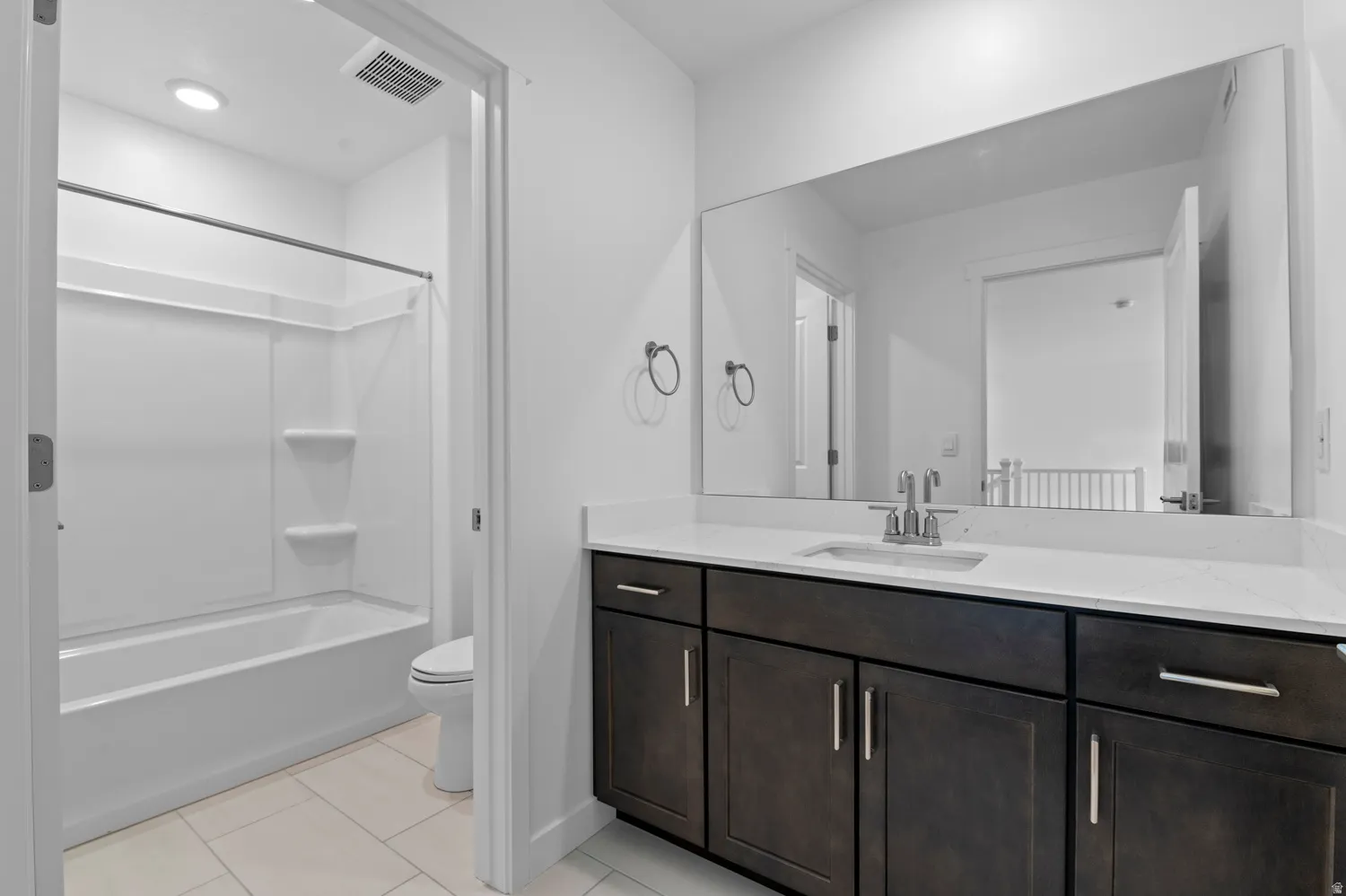 Bathroom featuring a white subway tile floor, a built-in shower and tub combination, a dark wood-finish vanity with a white countertop, and a large wall-mounted mirror