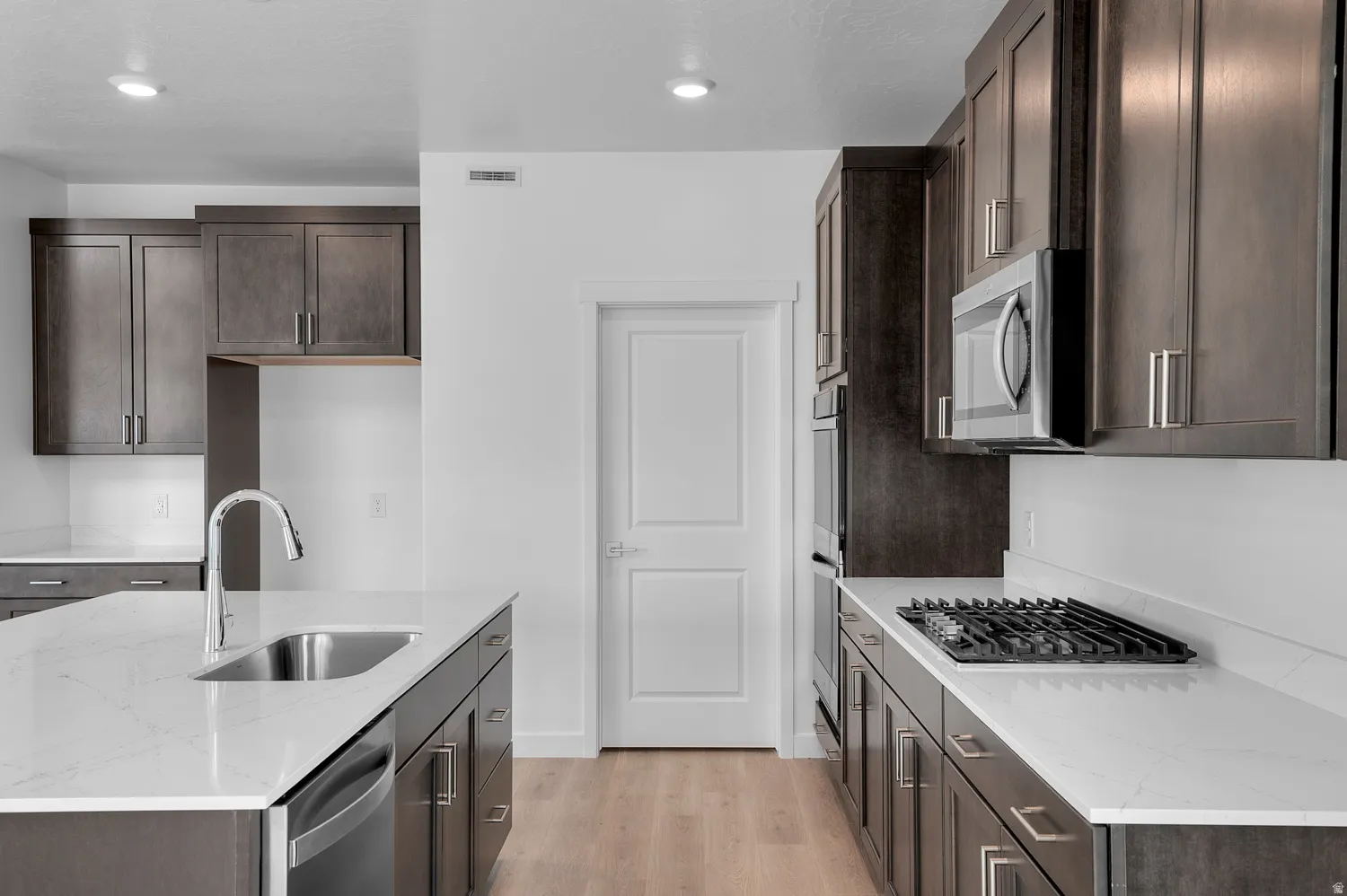 Kitchen featuring dark wood-finish cabinetry, light countertops, stainless steel appliances, a center island with sink, and wood-finish flooring