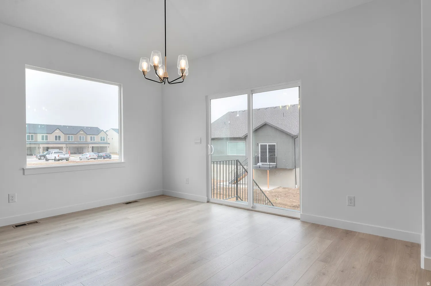 Open-concept interior featuring wood-finish flooring, a contemporary chandelier, a large picture window, and sliding glass doors with direct outdoor access