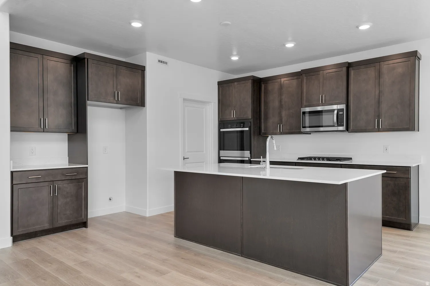 Spacious kitchen featuring dark wood-finish cabinetry, light countertops, stainless steel appliances, a large center island, and wood-finish flooring