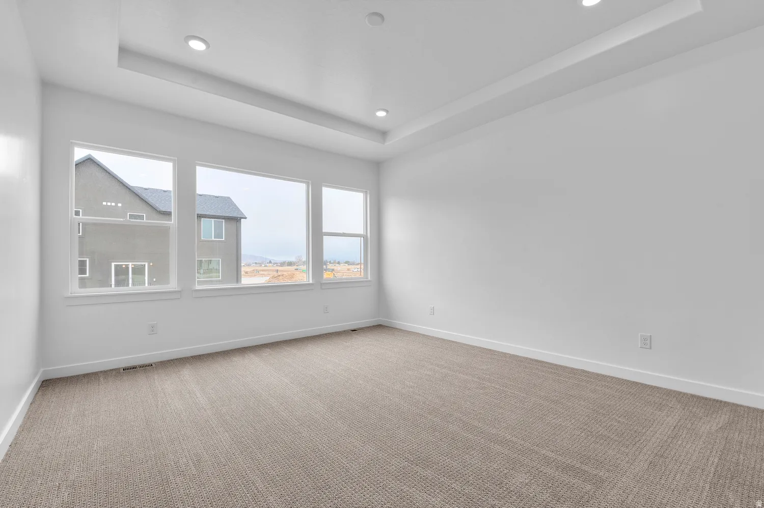 Tray ceiling with recessed lighting, light-toned carpet flooring, and a wall of three large windows