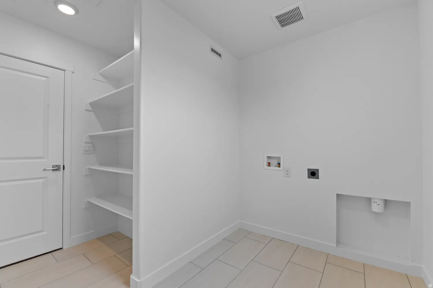 Recessed ceiling light, built-in shelving, panel door with lever hardware, and light-toned tile flooring