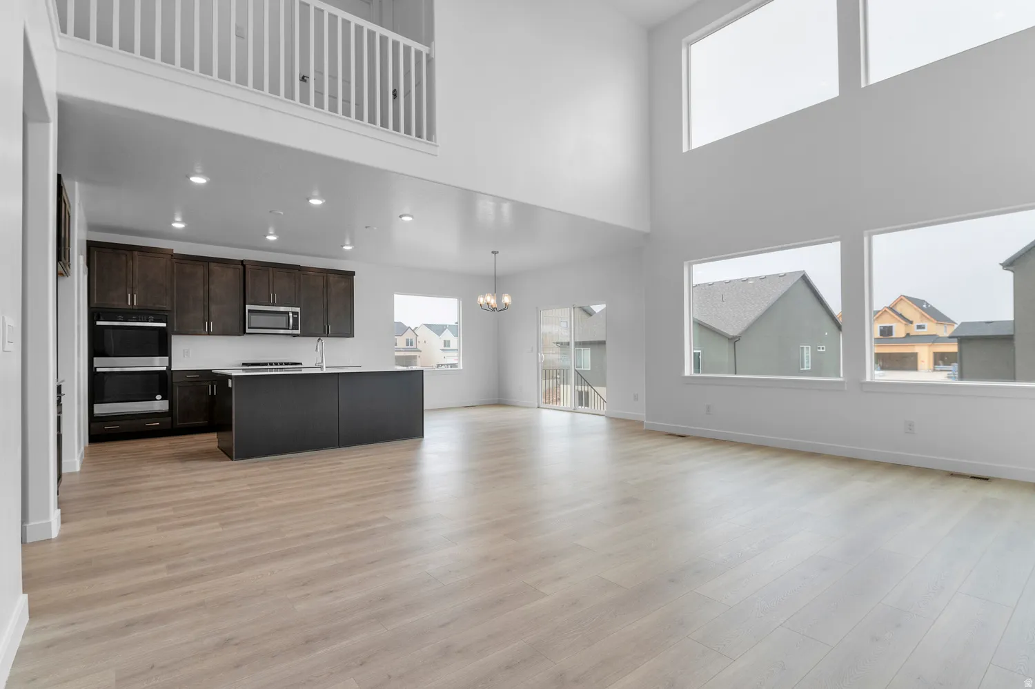 Open-concept living space with a soaring vaulted ceiling, extensive window placement, wood-finish flooring, and a kitchen featuring dark wood cabinetry and built-in appliances