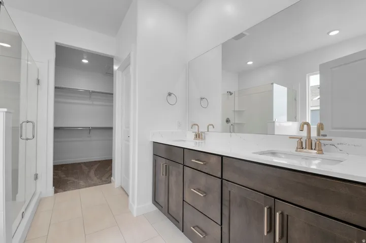 Dual vanity with integrated sinks and quartz countertops, wood-finish cabinetry, brushed gold hardware, and a walk-in shower with a glass enclosure