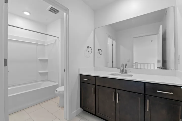 Bathroom featuring a white subway tile floor, a built-in shower and tub combination, a dark wood-finish vanity with a white countertop, and a large wall-mounted mirror