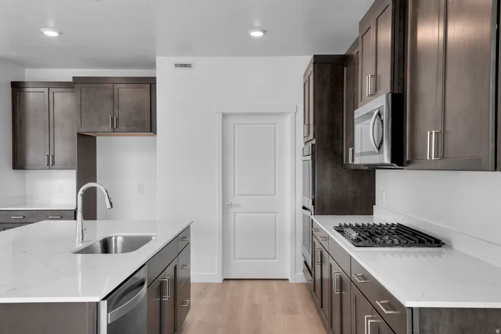 Kitchen featuring dark wood-finish cabinetry, light countertops, stainless steel appliances, a center island with sink, and wood-finish flooring