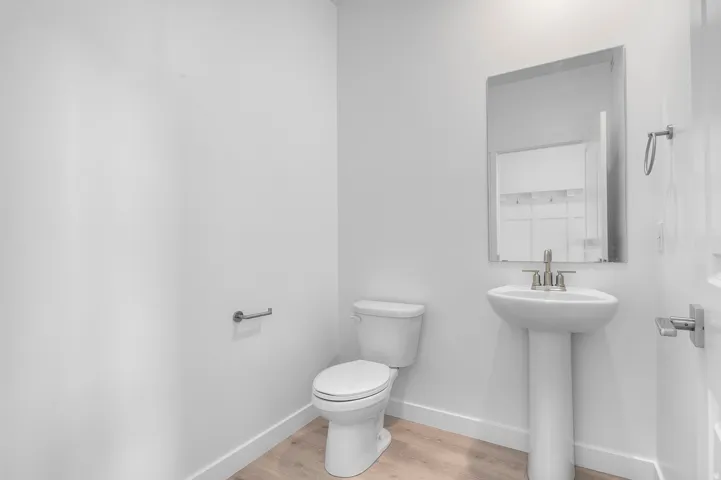 Pedestal sink with a polished chrome faucet, rectangular wall-mounted mirror, and wood-finish flooring