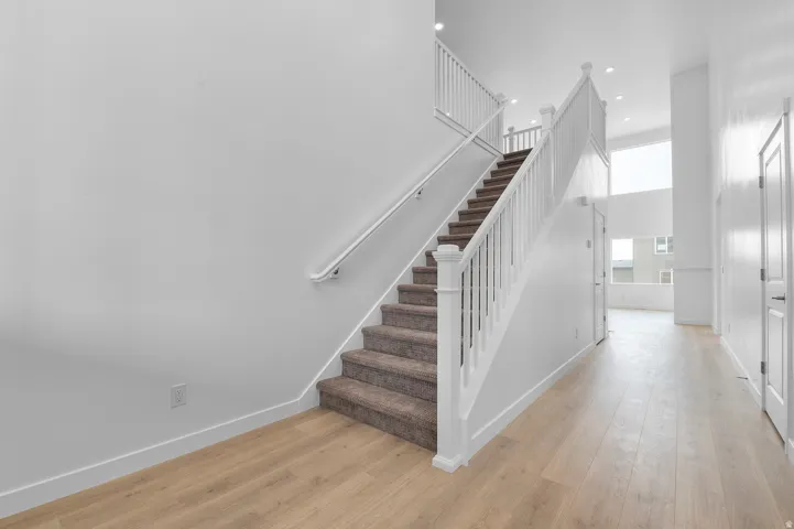 Wood-finish flooring, staircase with carpeted treads, white railing, and recessed lighting