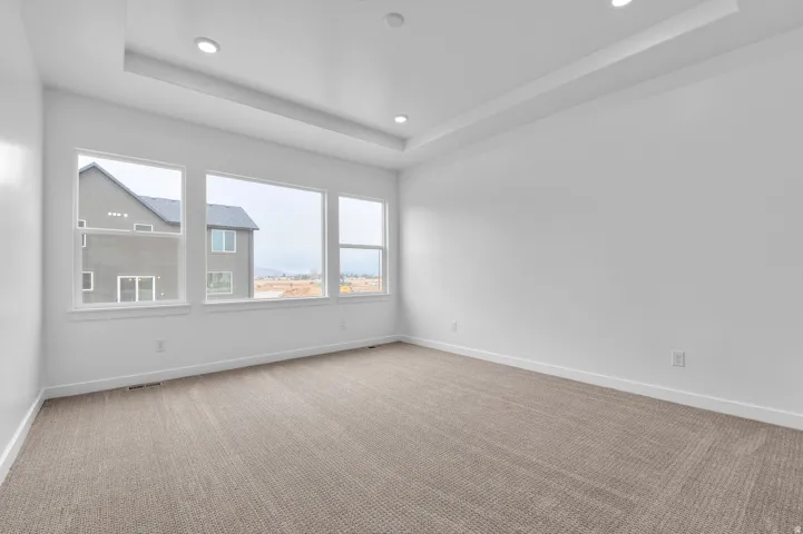 Tray ceiling with recessed lighting, light-toned carpet flooring, and a wall of three large windows
