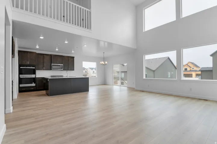 Open-concept living space with a soaring vaulted ceiling, extensive window placement, wood-finish flooring, and a kitchen featuring dark wood cabinetry and built-in appliances