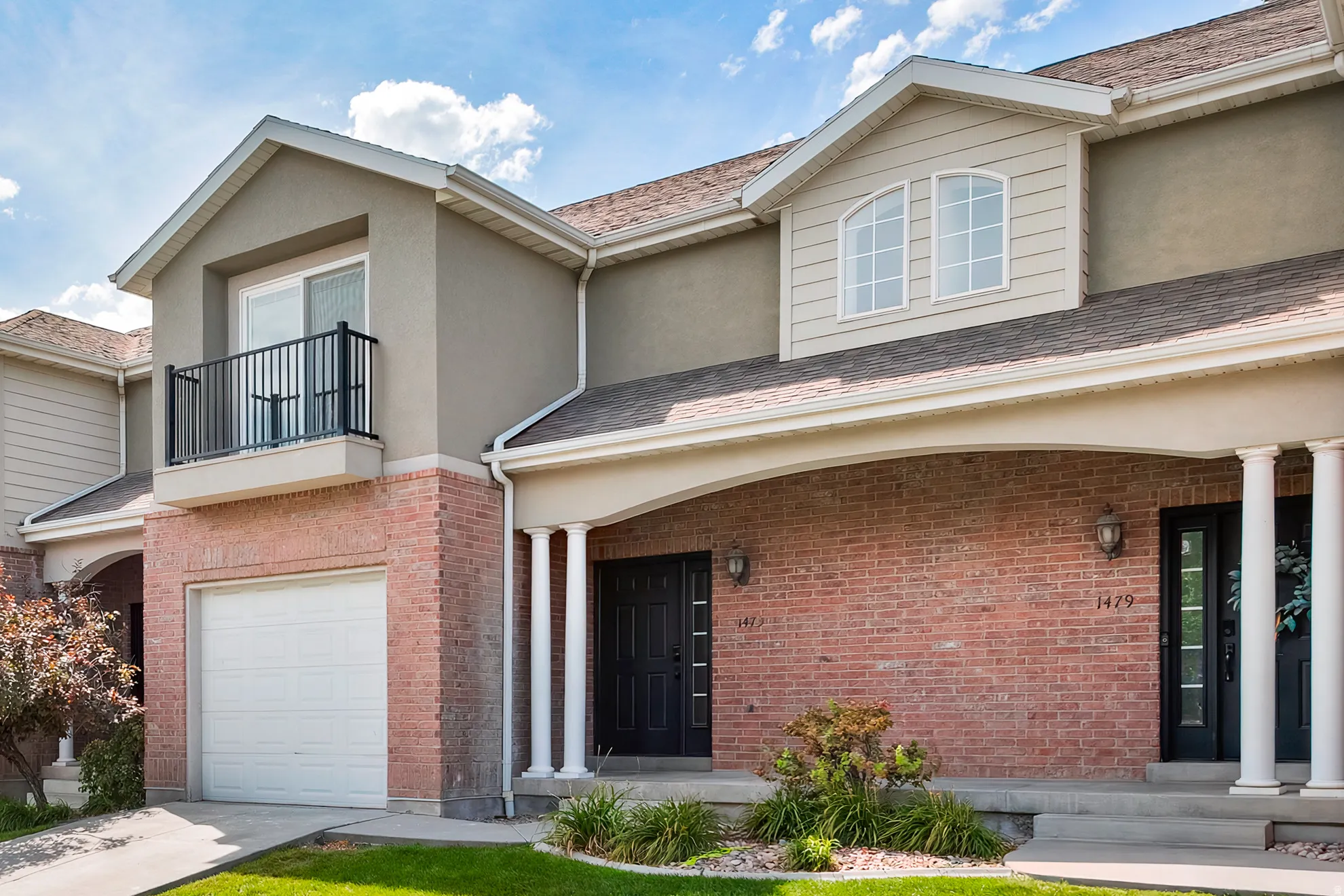 Brick and stucco exterior with an arched entryway, dormer window, and a second-story balcony