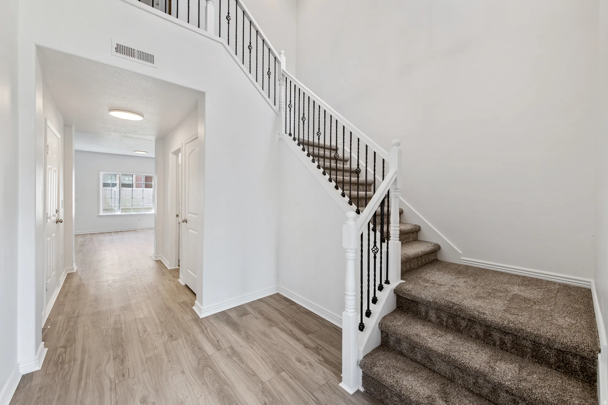 Entryway featuring wood-finish flooring, a carpeted staircase with decorative metal balusters, and a bright overhead light fixture