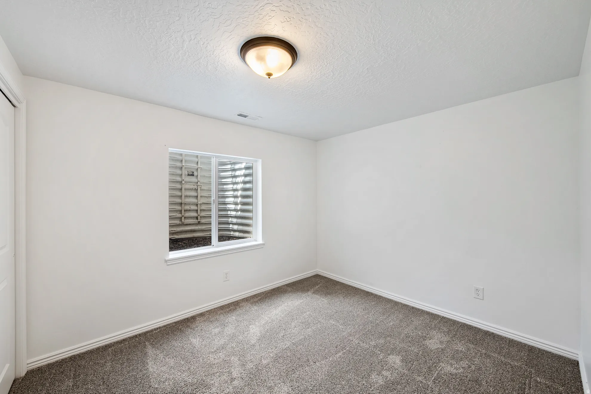 Neutral paint palette, textured ceiling, flush mount lighting, gray carpeting, and a window well with a sliding window