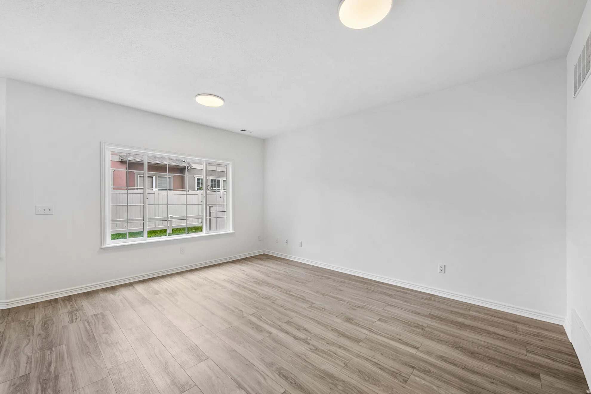 Spacious room featuring wood-finish flooring, white walls, and a large window with white muntins