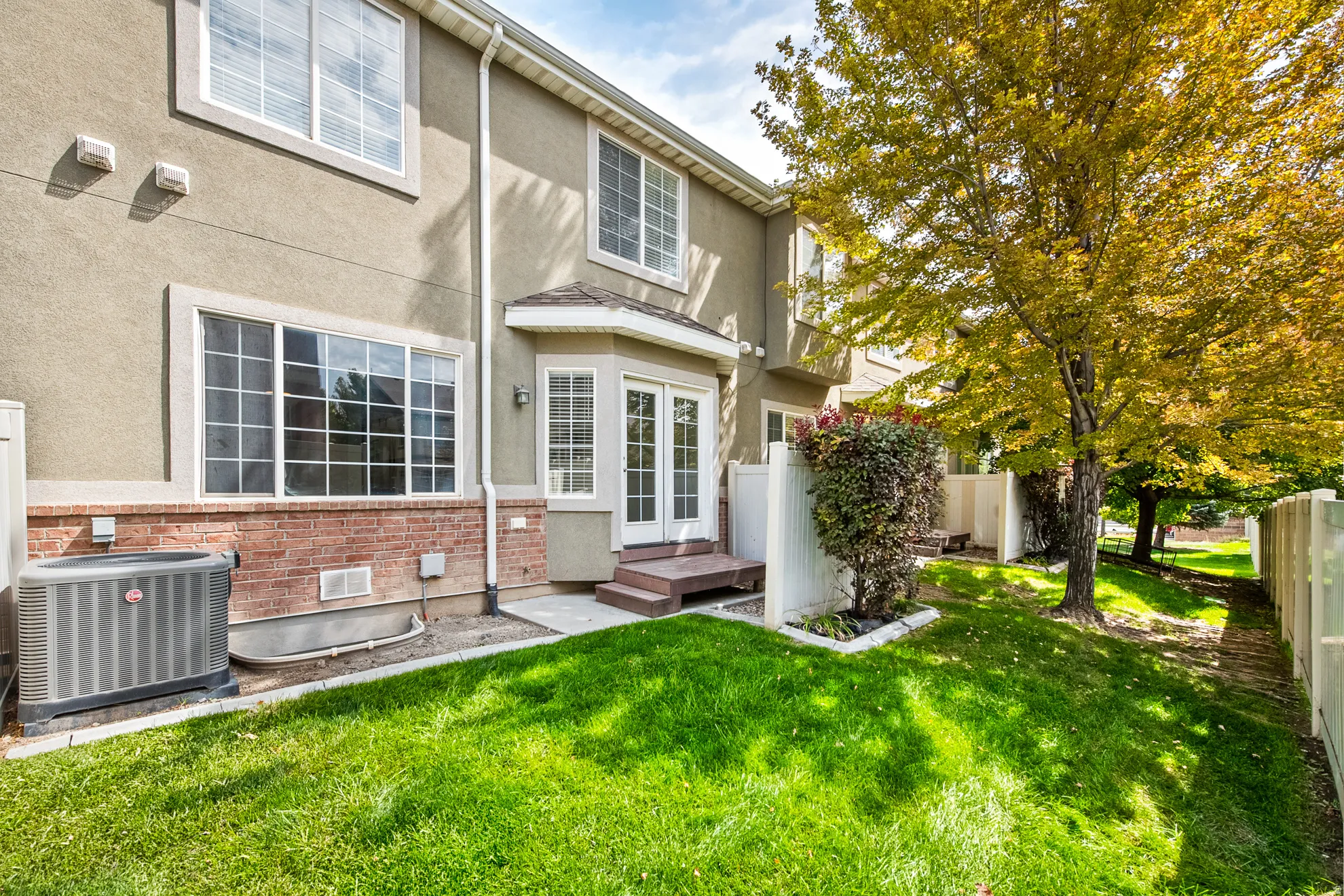 Rear exterior featuring stucco and brick siding, multiple windows, French doors with a bay window, and a grass lawn with mature trees