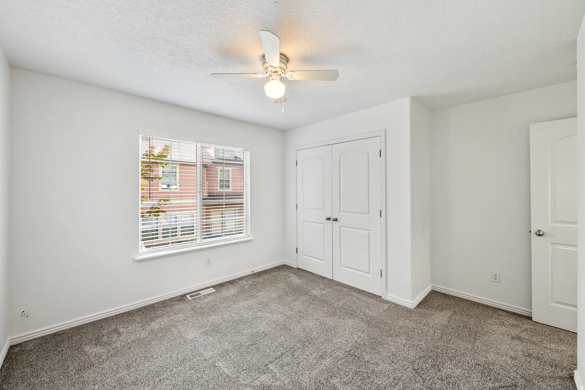 Neutral wall paint, carpet flooring, a window with horizontal blinds, bi-fold closet doors, and a ceiling fan with integrated lighting