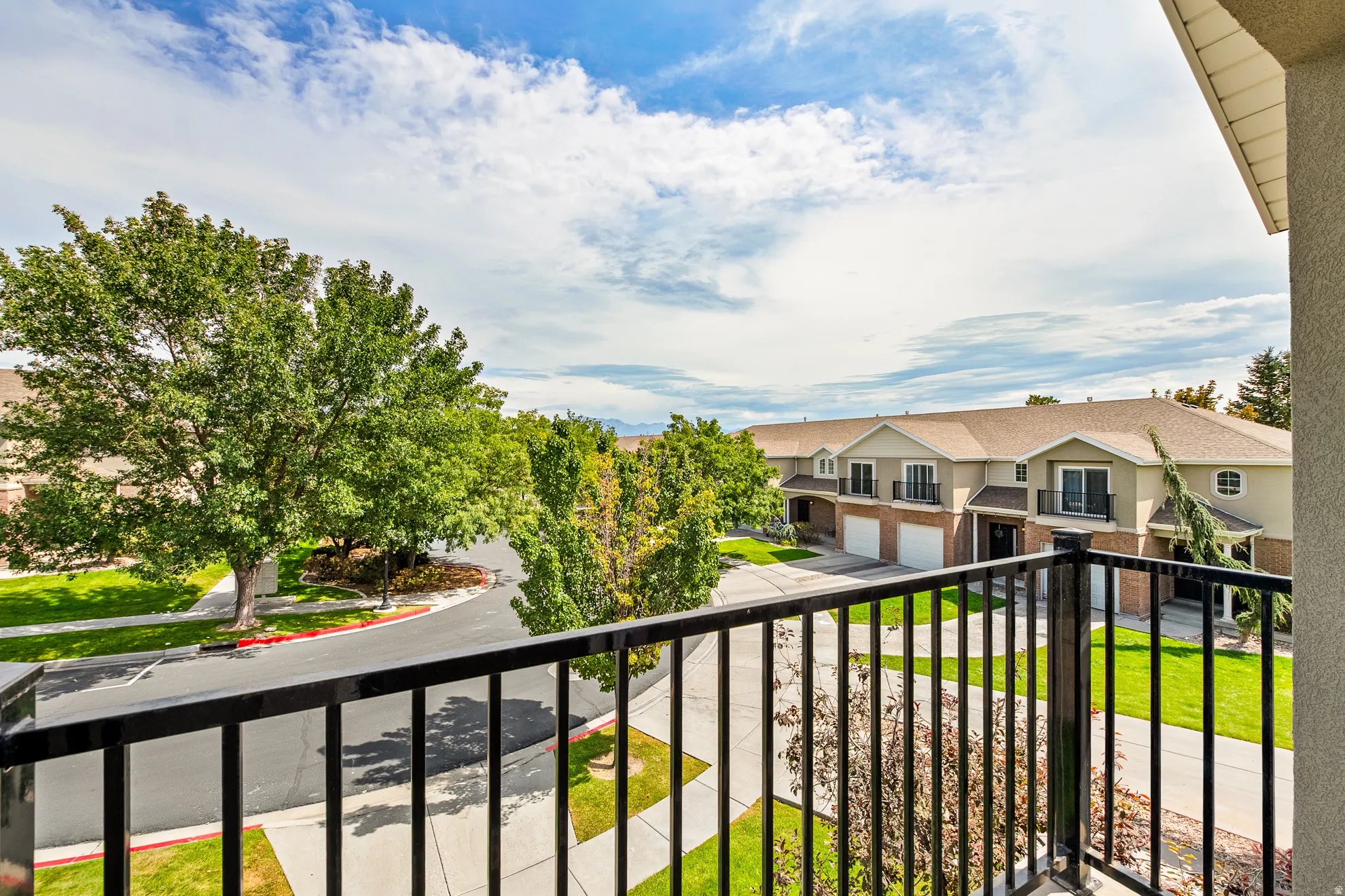 Black metal balcony railing overlooking a paved street, green lawns, and mature trees