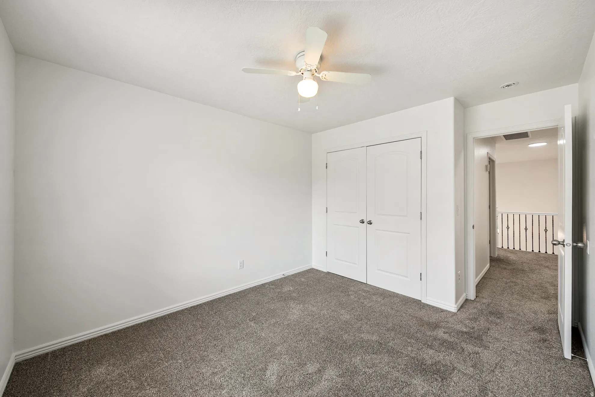 White walls, gray carpet, and a ceiling fan with integrated lighting