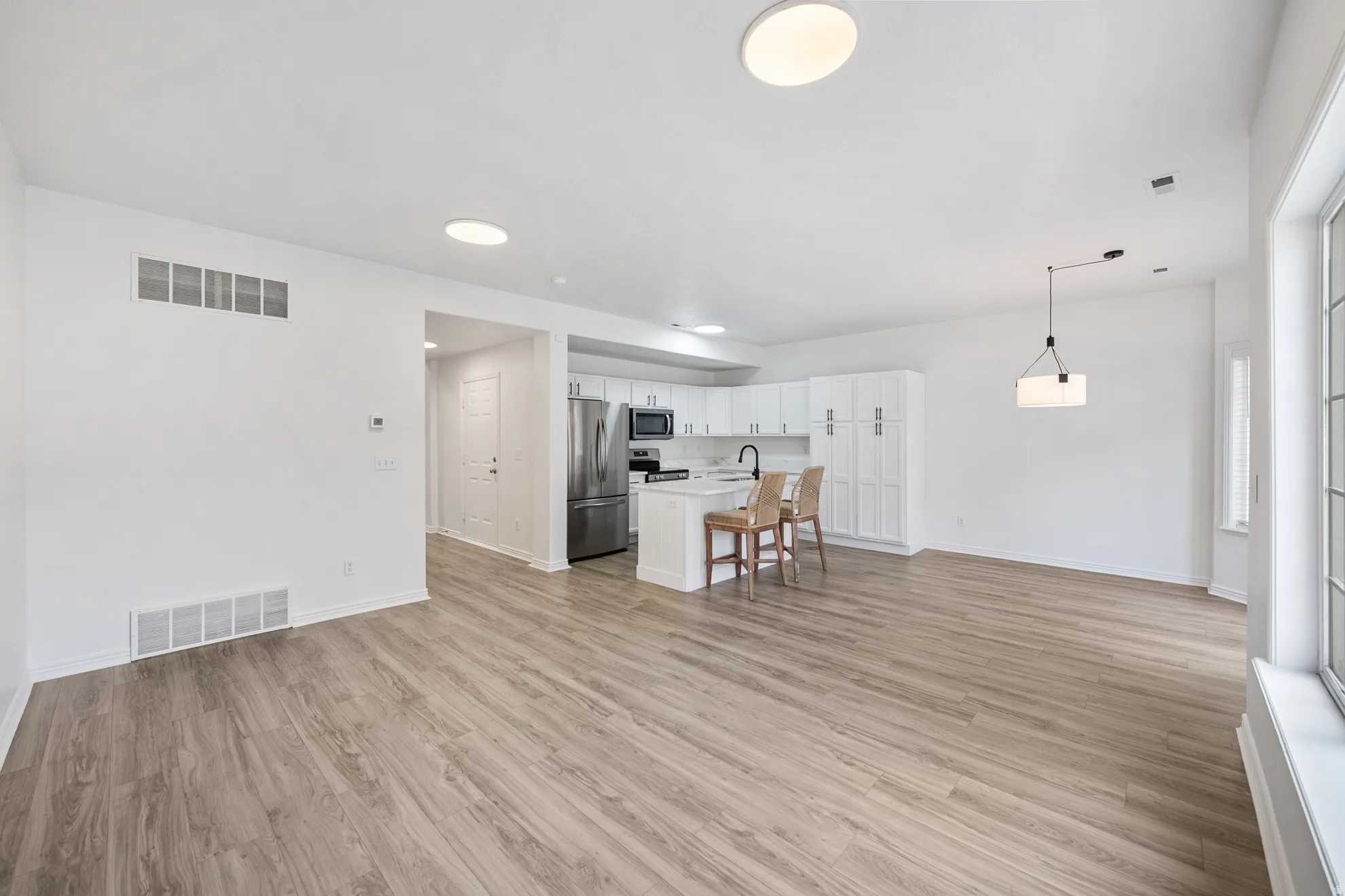 Open-concept living area with wood-finish flooring, recessed lighting, and a modern kitchen featuring white cabinetry, a center island, and stainless steel appliances