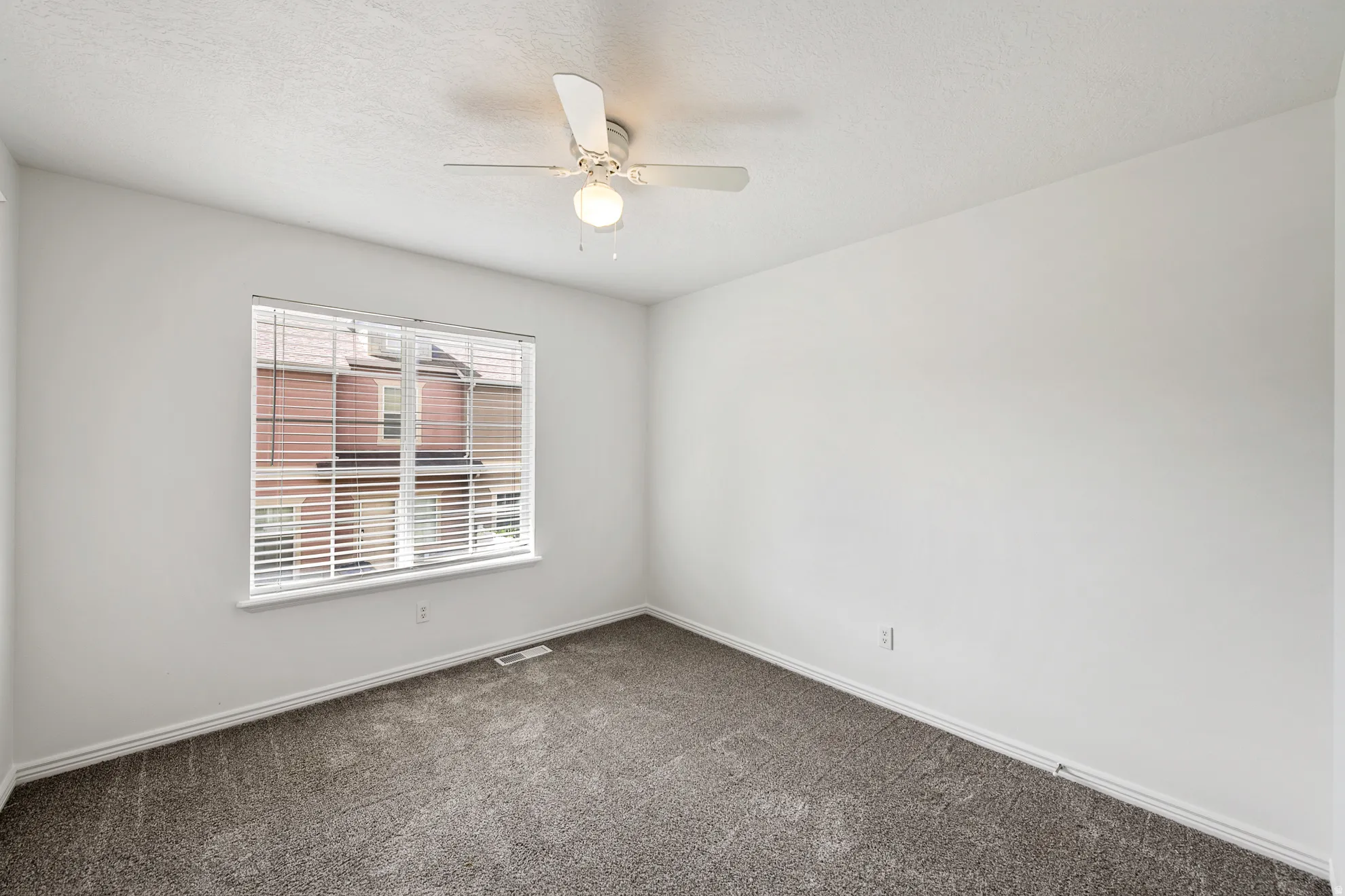 Neutral wall finishes with a textured ceiling, a window with horizontal blinds, and a ceiling fan with integrated lighting