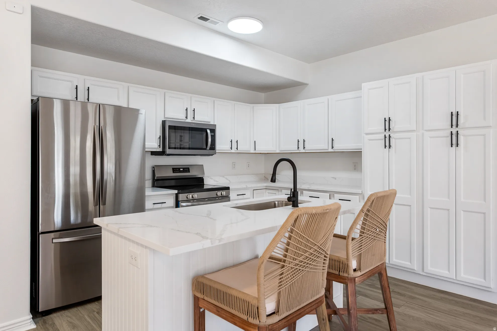 Kitchen featuring stainless steel appliances, white cabinetry with dark hardware, a center island with countertop seating, a single basin sink with a gooseneck faucet, and wood-finish flooring