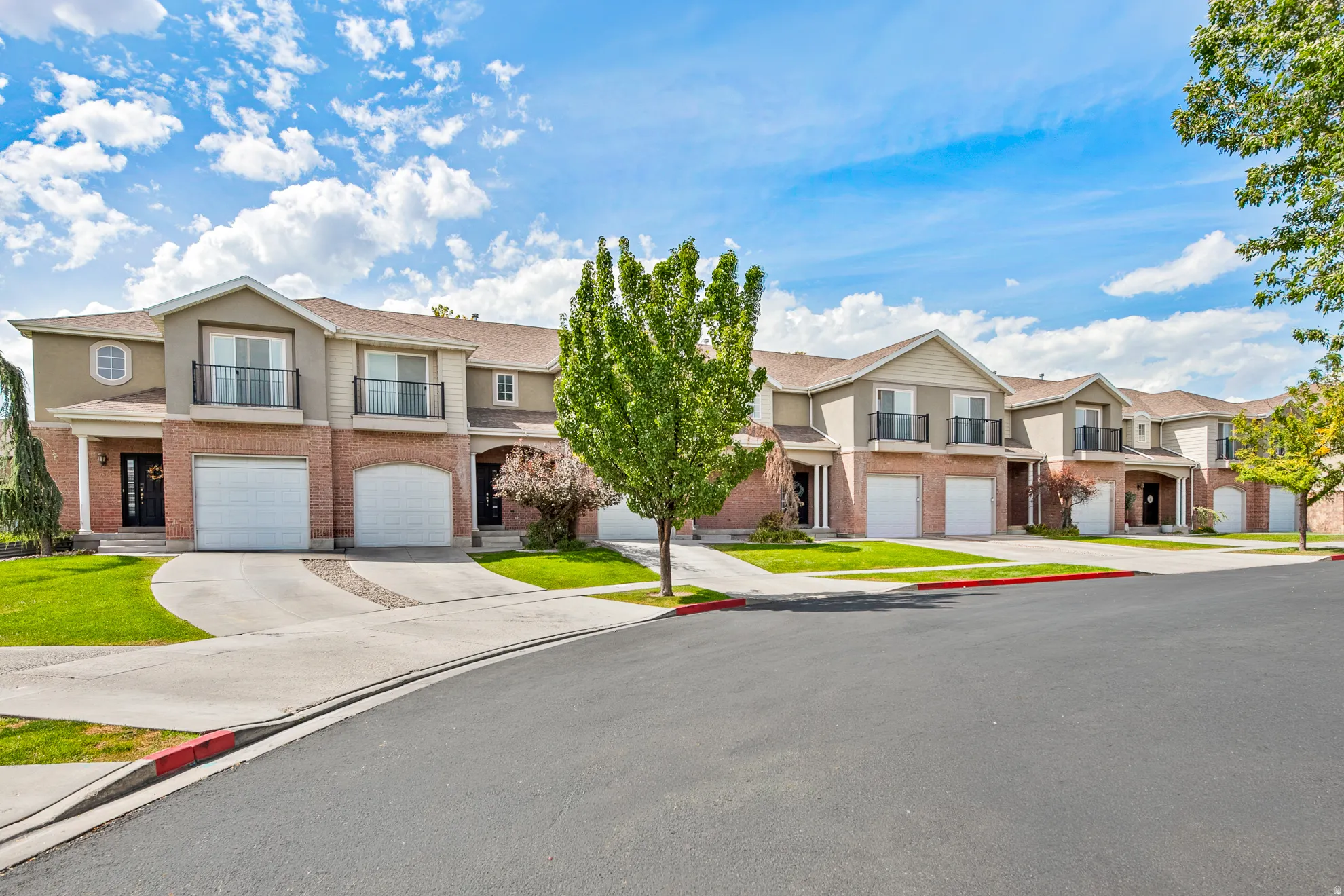 Brick and stucco exterior, arched garage doors, private balconies, paved driveways, and manicured lawns