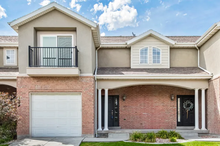 Brick facade with stucco accents, arched entryway with white columns, attached garage, and second-story balcony with metal railing