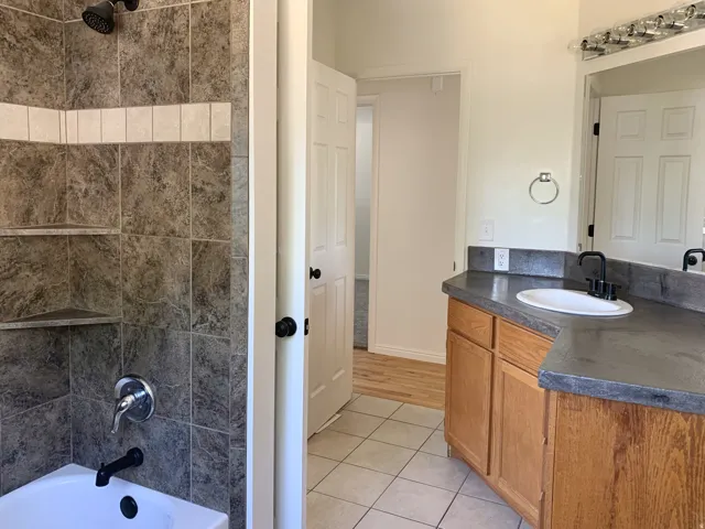 Bathroom featuring a tiled tub/shower combination with built-in shelving, dark-finish plumbing fixtures, a vanity with a drop-in sink, and wood-finish cabinetry