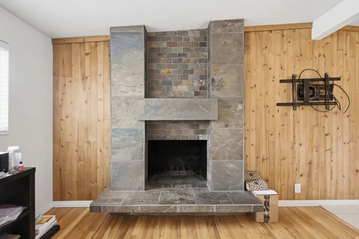 Stone-clad fireplace with a hearth, wood-finish flooring, and natural wood paneling