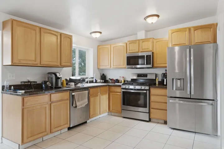 Recessed lighting, wood-finish cabinetry, stainless steel appliances, dark countertops, and tile flooring