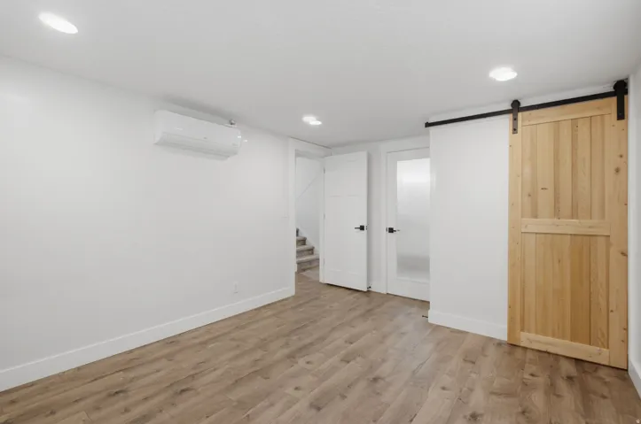 Wood-finish flooring, recessed ceiling lights, white walls, and a sliding barn door with black hardware