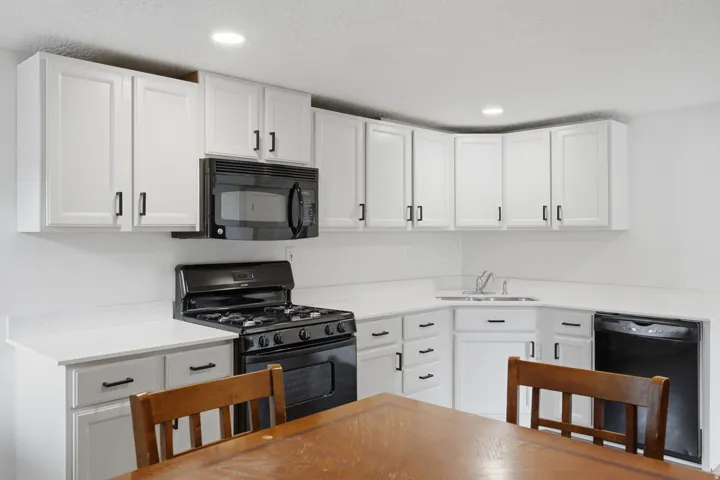 Kitchen featuring white cabinetry, black hardware, black appliances, solid surface countertops, and recessed lighting