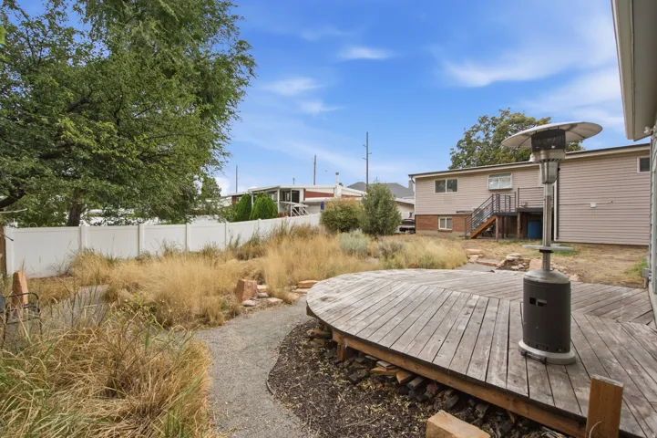 Expansive backyard featuring a large tree, white privacy fence, gravel pathway, and a multi-level wooden deck