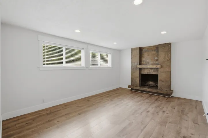 Wood-finish flooring, recessed lighting, stone-clad fireplace, and multiple windows with blinds