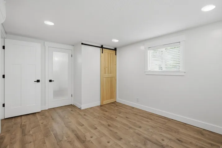 Wood-finish flooring, recessed lighting, white interior doors with matte black hardware, natural wood barn door, and a single window with blinds